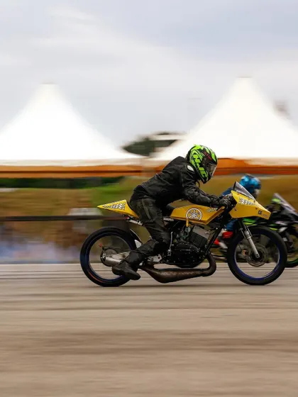 A classic yellow two-stroke race bike, likely a modified Yamaha RX, competing on the strip. We celebrate all eras of motorsport, from modern superbikes to iconic classics.