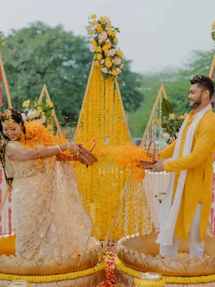 A couple having fun with a flower shower during their Haldi ceremony, seated in traditional lotus-shaped urlis.
