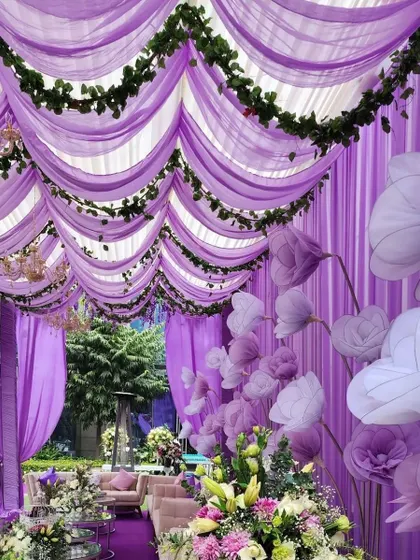 An imaginative ceiling decor using purple organza drapes and large, handmade paper flowers to create a whimsical lounge area.