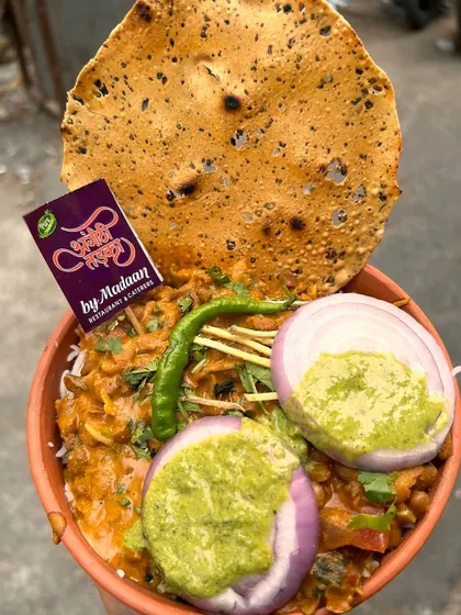 A close-up of our delicious Rajma Chawal served in an earthen bowl, topped with fresh onions, green chutney, and a crispy papad. It's a simple yet incredibly satisfying meal.