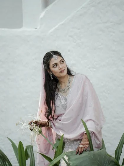 A duplicate of a beautiful portrait of a bride in a soft pink outfit, her thoughtful expression captured as she holds a delicate white flower.