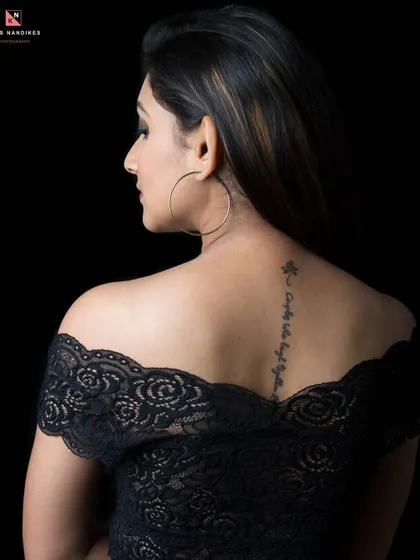 A portrait focusing on the model's back, showcasing a delicate tattoo along her spine. The off-shoulder lace top and the dramatic studio lighting create an intimate and artistic shot.