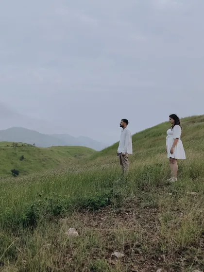 A wide, atmospheric shot of the couple looking out over a vast green valley, creating a sense of contemplation and shared dreams.