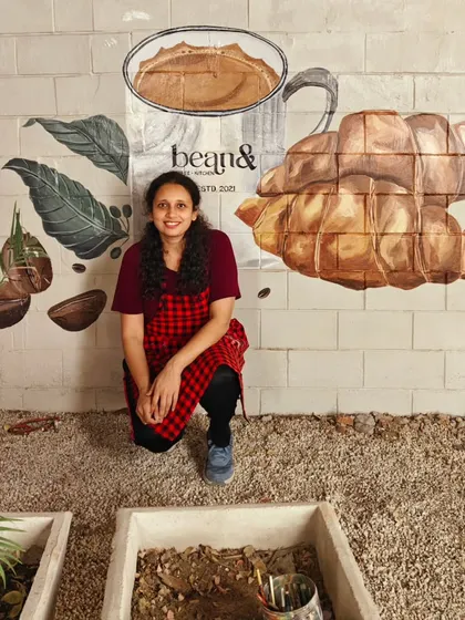 Posing with the completed mural at 'bean&' cafe. The artwork combines realistic depictions of coffee and croissants with the cafe's logo, making it a perfect backdrop for photos.