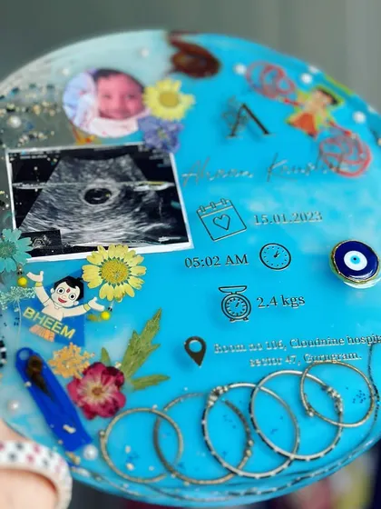 A detailed close-up of the baby keepsake. You can see the tiny rakhi, the nazar battu, and the carefully placed flowers, all coming together to create a beautiful and protective piece for the little one.