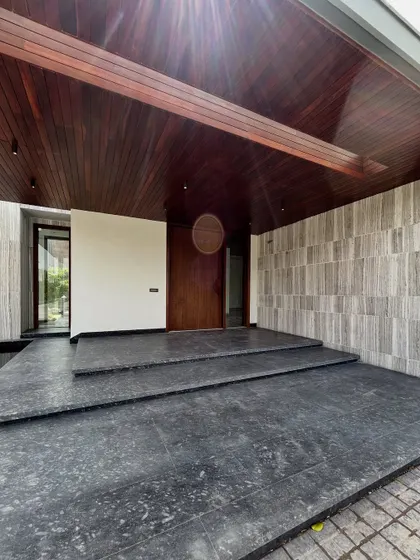 The entryway at Rosewood Farmhouse is raised on broad steps, with an oversized covered porch that balances the facade. Warm wood details soften the grey stone, creating a welcoming contrast that sets a grand yet grounded tone.