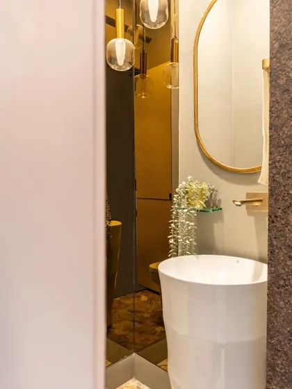 A glimpse into a glamorous powder room. The gold-tinted mirror, sculptural sink, and dramatic pendant lights create a jewel-box effect, proving that small spaces can have a huge impact.