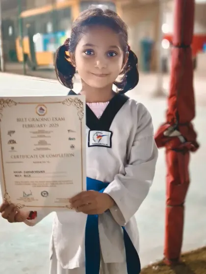 A young student proudly holds her certificate for achieving the blue belt. This is a significant milestone in her Taekwondo journey.