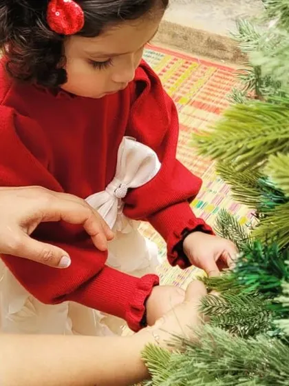 A little one carefully places an ornament with a helping hand from an adult. Our celebrations are intergenerational, bringing the entire school family together to create joyful memories.