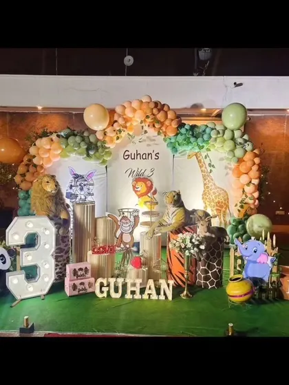 We created a complete jungle safari for Guhan's third birthday. The decor includes large animal props like a lion, tiger, and giraffe, along with a balloon arch in earthy tones and a personalized "Wild 3" backdrop.