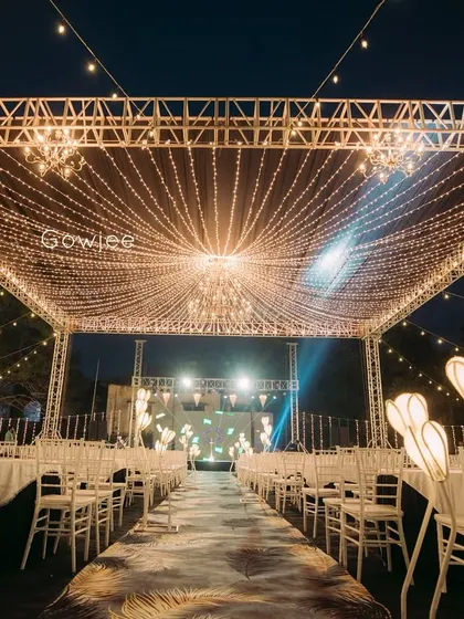 An elegant outdoor reception setup with a patterned aisle runner and a canopy of fairy lights.