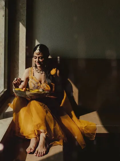 A stunning, artistic shot of the bride sitting by a window, the natural light highlighting her yellow outfit and the sunny decor theme.