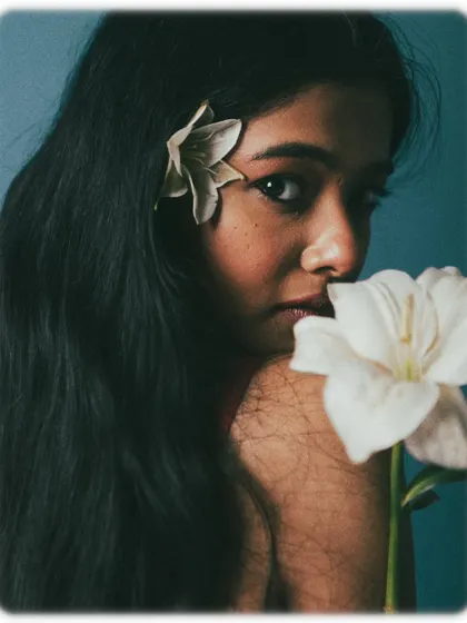 A moody and artistic portrait using flowers as a key element. The lighting is dark and dramatic, creating a sense of mystery.