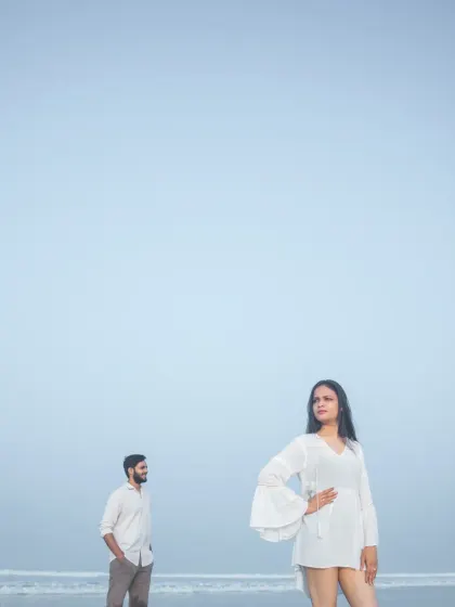 A stylish and moody beach portrait with a wide expanse of blue sky. The composition creates a sense of space and freedom, perfect for a modern pre-wedding album.