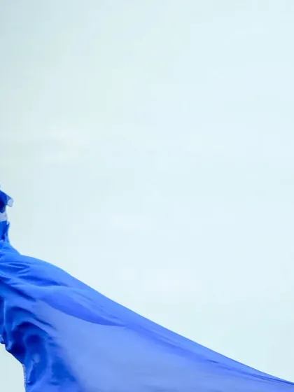 The flowing trail of a royal blue gown against a clear sky.