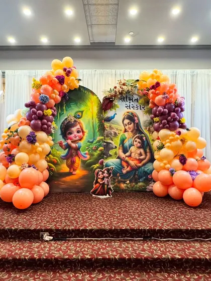 A Seemantha Sanskar ceremony setup with a backdrop featuring baby Krishna and Yashoda. The decor is brought to life with a colorful balloon arch in shades of orange, peach, and purple, perfectly complementing the artwork.