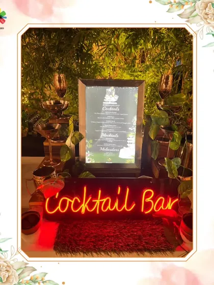A close-up of our cocktail bar, featuring a custom neon sign, elegant glassware, and a framed menu. The surrounding greenery adds a touch of natural beauty to the setup.