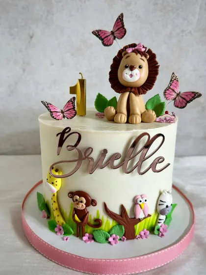 A perfectly adorable jungle cake for a little girl's first birthday. This design features a sweet lioness topper, pretty pink butterflies, and a delicate animal border.