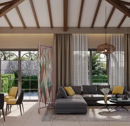 The living room of a Goa villa, featuring a high, pitched ceiling with exposed wooden beams. The space is decorated with an eclectic fusion of colors and patterns, including pops of yellow and a vibrant folding screen, capturing a modern Goan spirit.