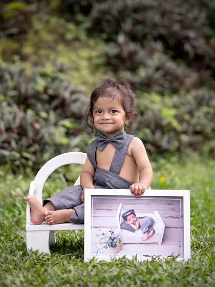 Another angle of the milestone shot, with the little boy sitting on a miniature bench in the grass, proudly displaying his newborn picture. A testament to a year of growth and love.