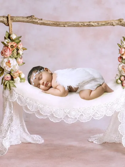 A one-month-old baby girl dressed as an angel, sleeping on a delicate lace hammock.