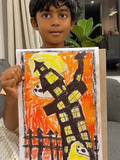 This Halloween artwork uses oil pastels to create a fiery orange sky behind a crooked haunted house, a fantastic piece by a talented online student.