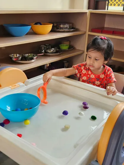 Using tongs to pick up wet pom-poms is a fun challenge that requires focus and dexterity. This practical life skill activity is a favorite among our toddlers.