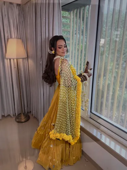 A full look of the bride in her yellow Haldi lehenga, complemented by the delicate, handcrafted Tagar bud dupatta with a marigold border.
