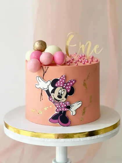 This modern Minnie Mouse cake uses a 2D character design against a peach-coloured buttercream. The balloon-like spheres and gold details give it a contemporary and stylish look.