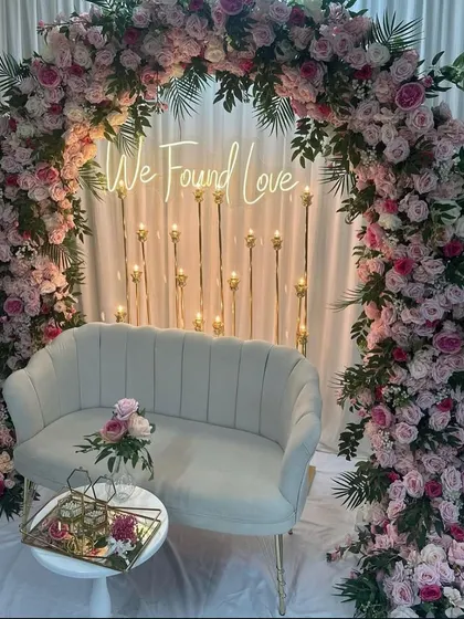 An elegant Roka ceremony backdrop with a "We Found Love" neon sign. The setup features a beautiful arch of pink and white roses.