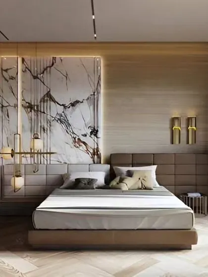 A luxurious bedroom design featuring a marble accent wall with brass inlays. The combination of an upholstered headboard, herringbone wood flooring, and designer lighting creates a high-end hotel feel.