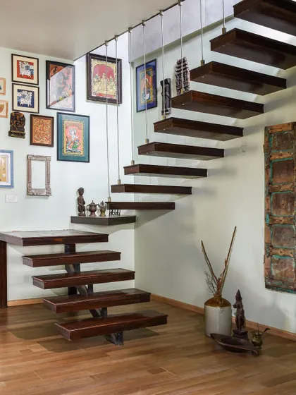 A stunning floating staircase made of dark wood, with a gallery wall of traditional Indian art beside it.