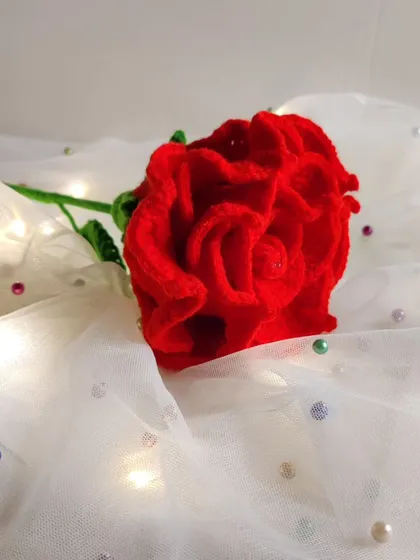 A slightly different angle of the crochet rose on the white fabric, with soft lighting.