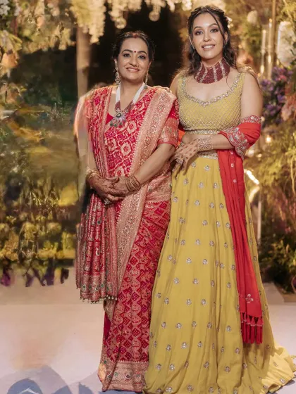Two generations celebrating together. On the left, a client wears my custom red Bandhani saree, and on the right, her daughter wears a vibrant yellow lehenga, showing the range of styles I create.