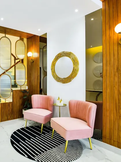 The entrance to a home should be a hint of the story that unfolds inside. Here, soft blush chairs, warm wood paneling, and a striking gold mirror create an inviting first impression. It’s a space that balances elegance with a touch of playful charm, promising more beauty within.
