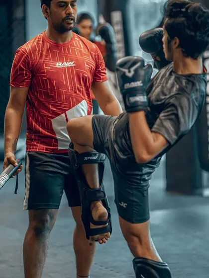 A young fighter practices his kick check while I hold a training stick. This is a crucial defensive move in Muay Thai, and we drill it relentlessly to make it second nature.