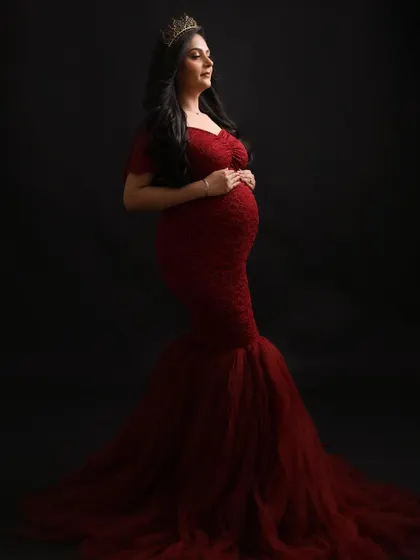 A profile of a queen. This elegant pose showcases the beautiful silhouette of the baby bump and the intricate details of the red lace gown.