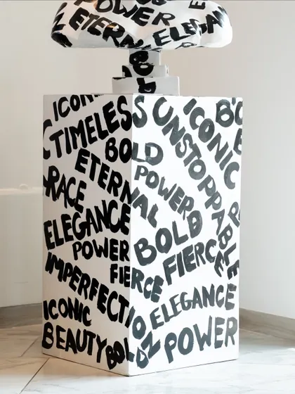 The base of the "Medusa: The Eternal Icon" sculpture, covered in empowering words like "Timeless," "Bold," and "Power."
