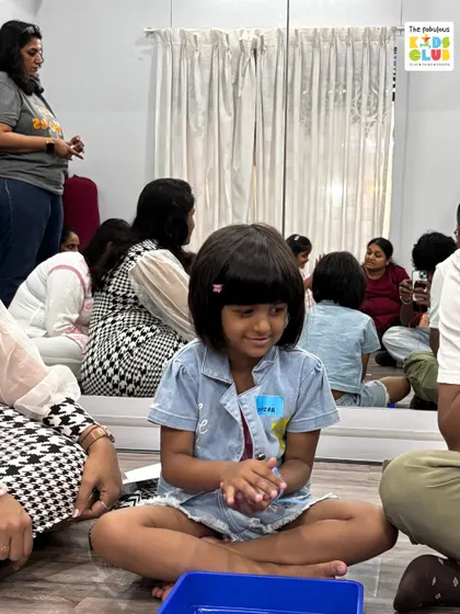 A child sits focused on a sensory play activity, surrounded by other children and parents. This captures the calm, community-focused environment of our club.