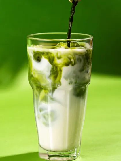 A mesmerizing shot of matcha being poured into milk against a bright green background. The swirling patterns create a beautiful and satisfying visual.