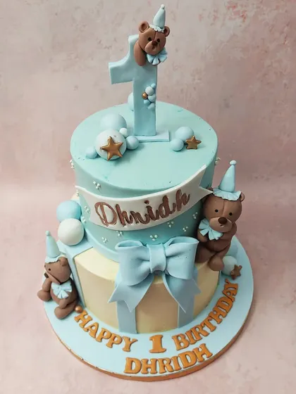 We design a classic and cuddly first birthday cake with this two-tiered teddy bear theme. Dressed in party hats and surrounded by blue and cream tones with a large bow, these teddy bears create a timeless and heartwarming centerpiece.