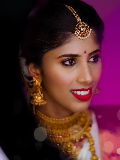 A striking portrait of the bride against a vibrant purple background, her gold jewelry and red lipstick creating a bold look.