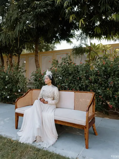 A serene solo portrait of the bride seated on a bench in a palace garden, looking poised and elegant in her white ensemble.