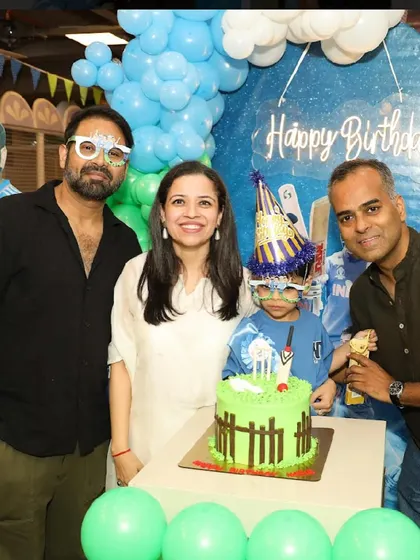The birthday boy and his family, wearing fun glasses, get ready to cut the cricket-themed cake.