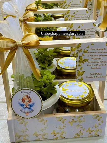 This image focuses on the contents of the announcement basket, including the "It's a girl" tag, a healthy plant, and jars of delicious treats.