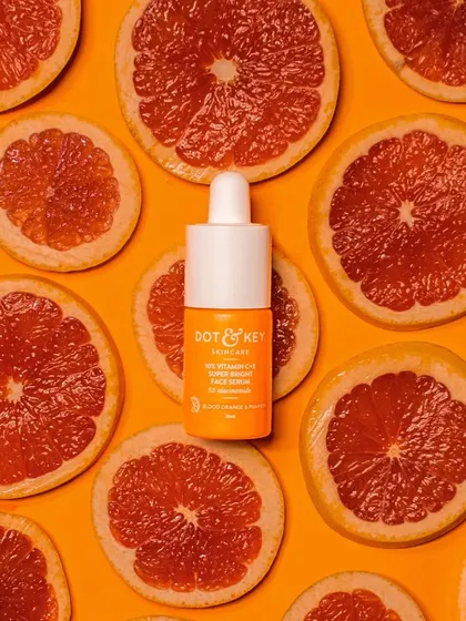 A vitamin C serum surrounded by slices of fresh grapefruit on a vibrant orange background. This flat-lay shot directly communicates the product's key ingredient and its zesty, energizing properties.