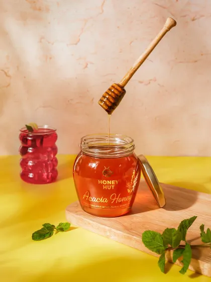 A sweet and sunny shot of Acacia Honey. The composition uses a wooden board, fresh mint, and a glass of iced tea to create a warm, inviting, and natural scene.