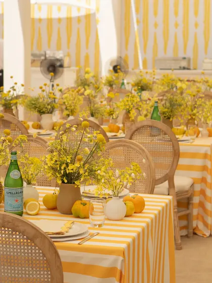 The tables were set with care, featuring striped linens, simple glassware, and beautiful arrangements of yellow wildflowers in rustic vases.