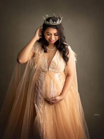 Adjusting her crown, this mom-to-be looks down at her bump with a gentle smile, looking absolutely radiant in her shimmering gown.
