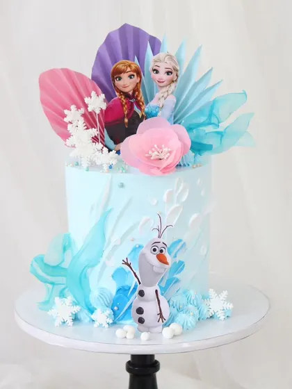 An artistic take on the "Frozen" theme, this cake features Elsa, Anna, and Olaf. The design is decorated with beautiful rice paper sails in shades of pink and blue, along with delicate snowflakes.